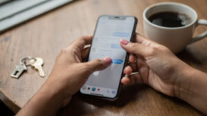 Tangan menaip mesej WhatsApp di telefon dengan kunci rumah di atas meja